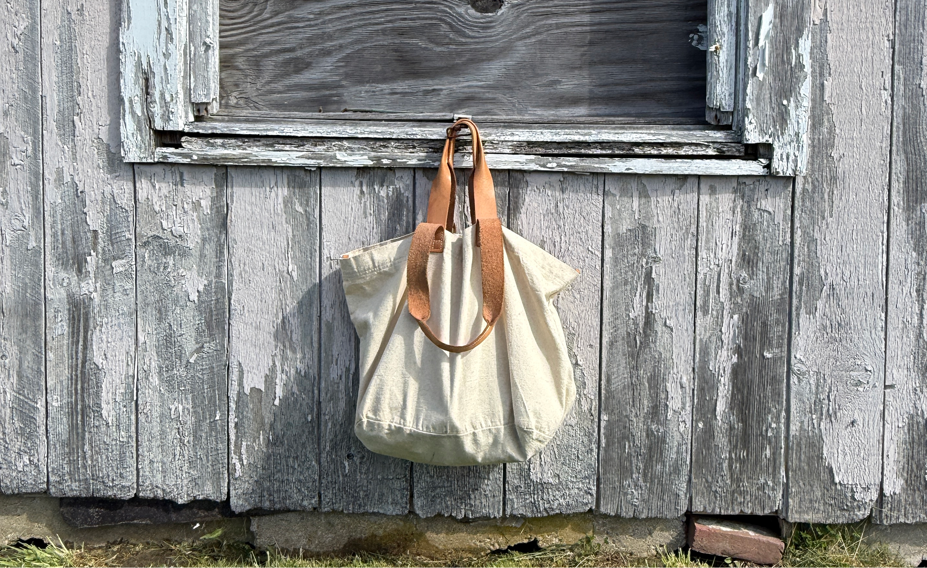 White tote bag with brown leather straps hanging on a wooden door