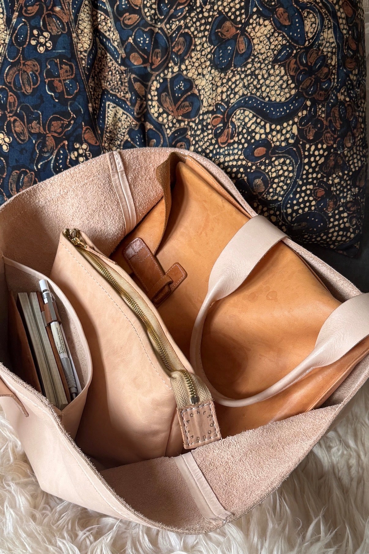 Large leather handbag with a brown leather strap and gold zipper on a textured surface. 