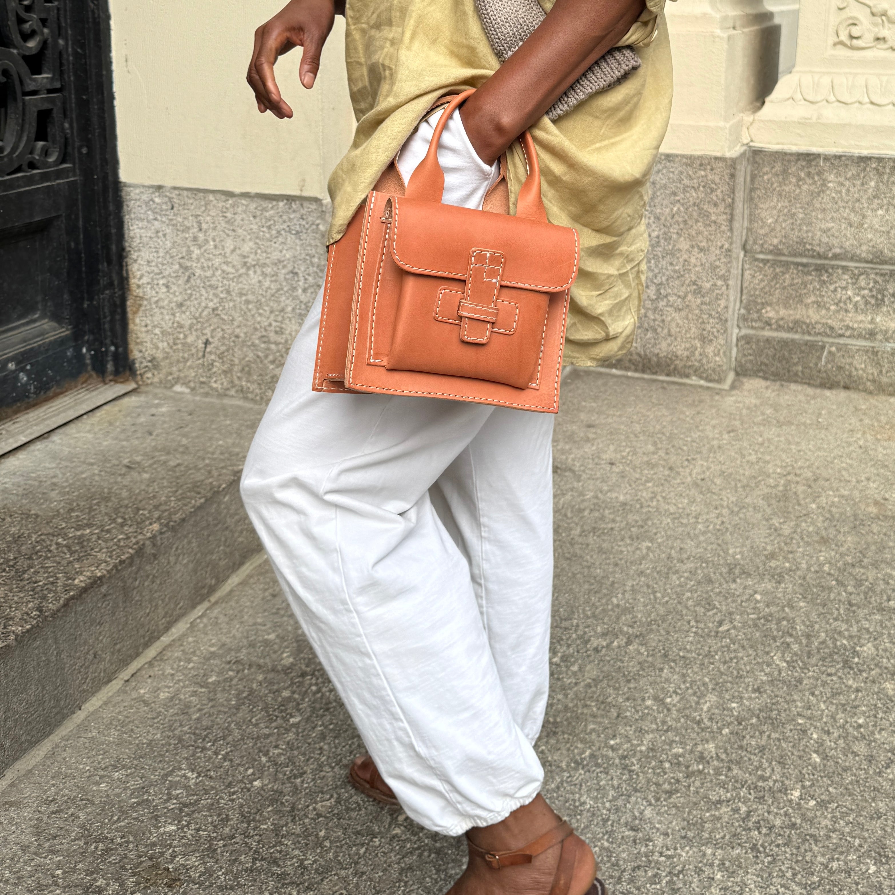 small leather bag being casually held. The women holding it has a hand in her pocket walking along the street. 