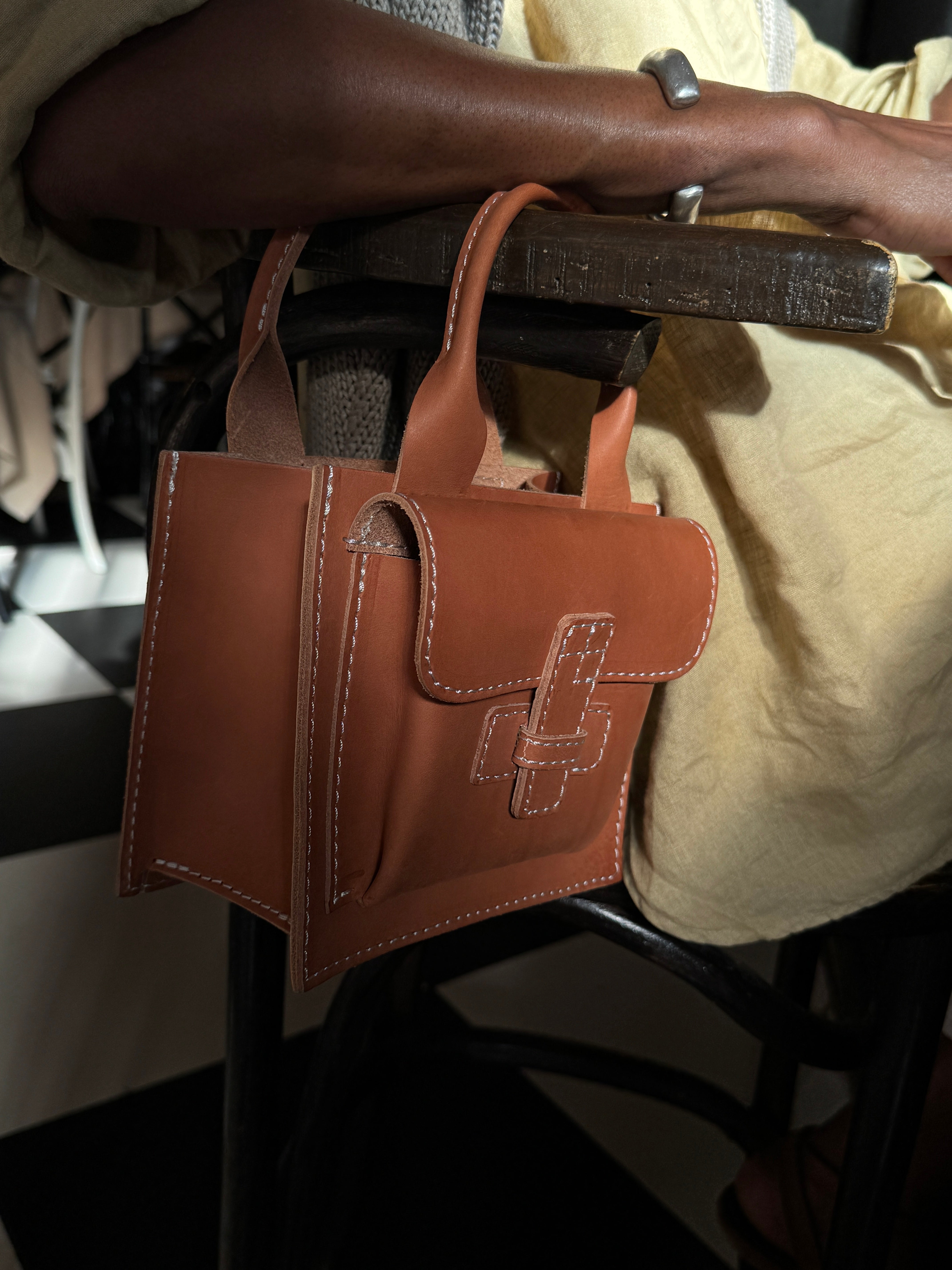 Honey colored, small, leather handbag hanging from a chair handle.
