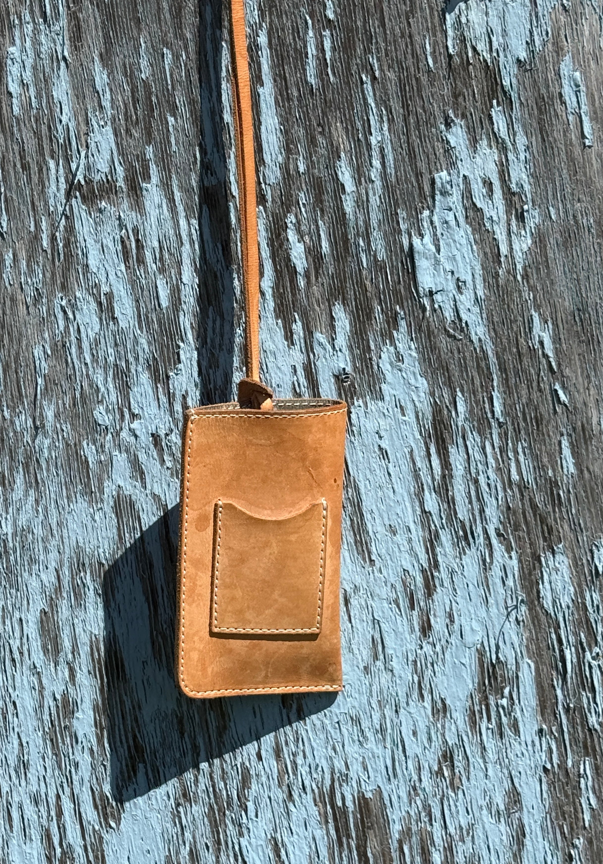 Brown leather phone case with strap on a textured wooden surface