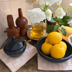 Bowl of lemons on a decorative stand with flowers and candles in the background.