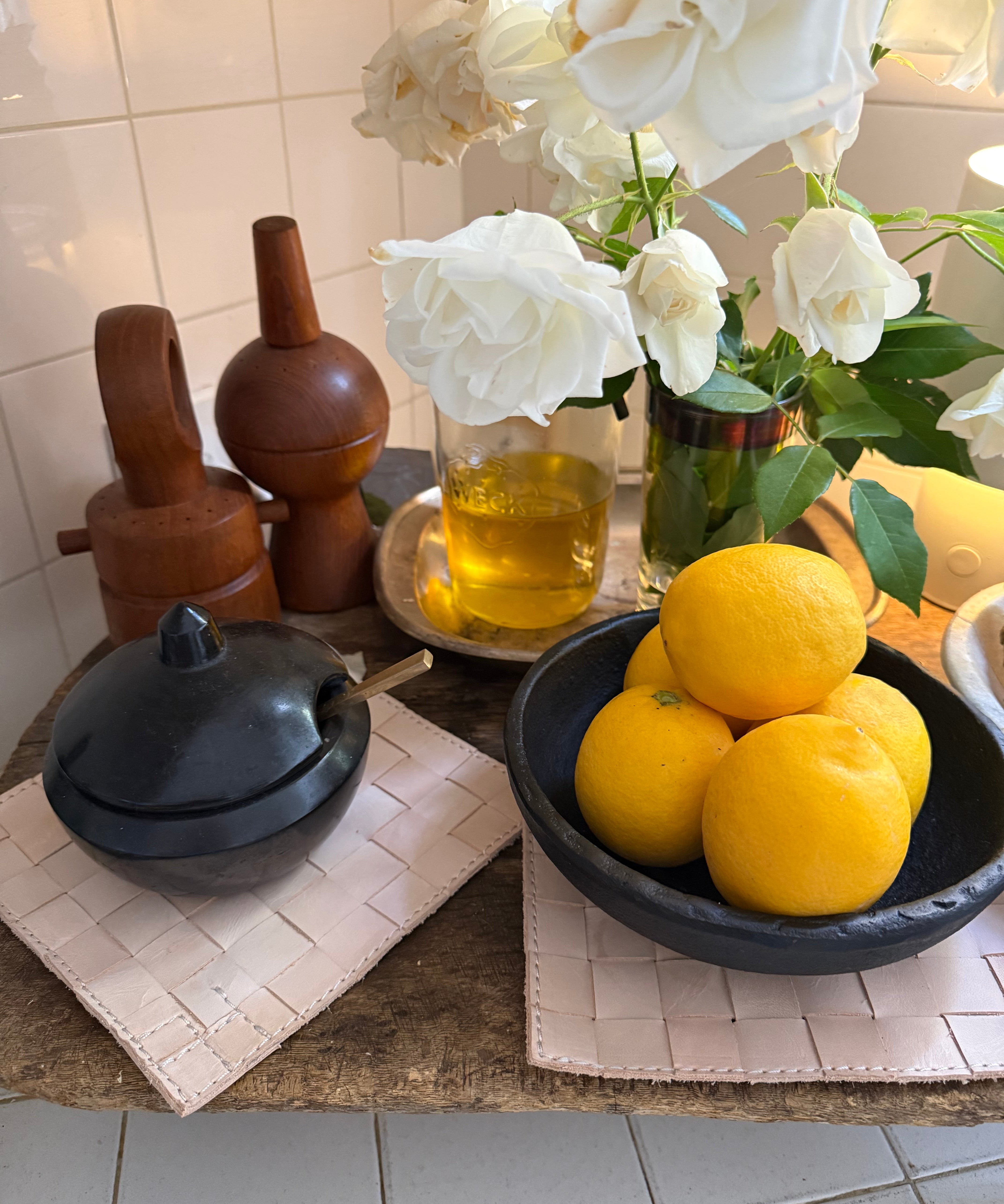 Bowl of lemons on a decorative stand with flowers and candles in the background.
