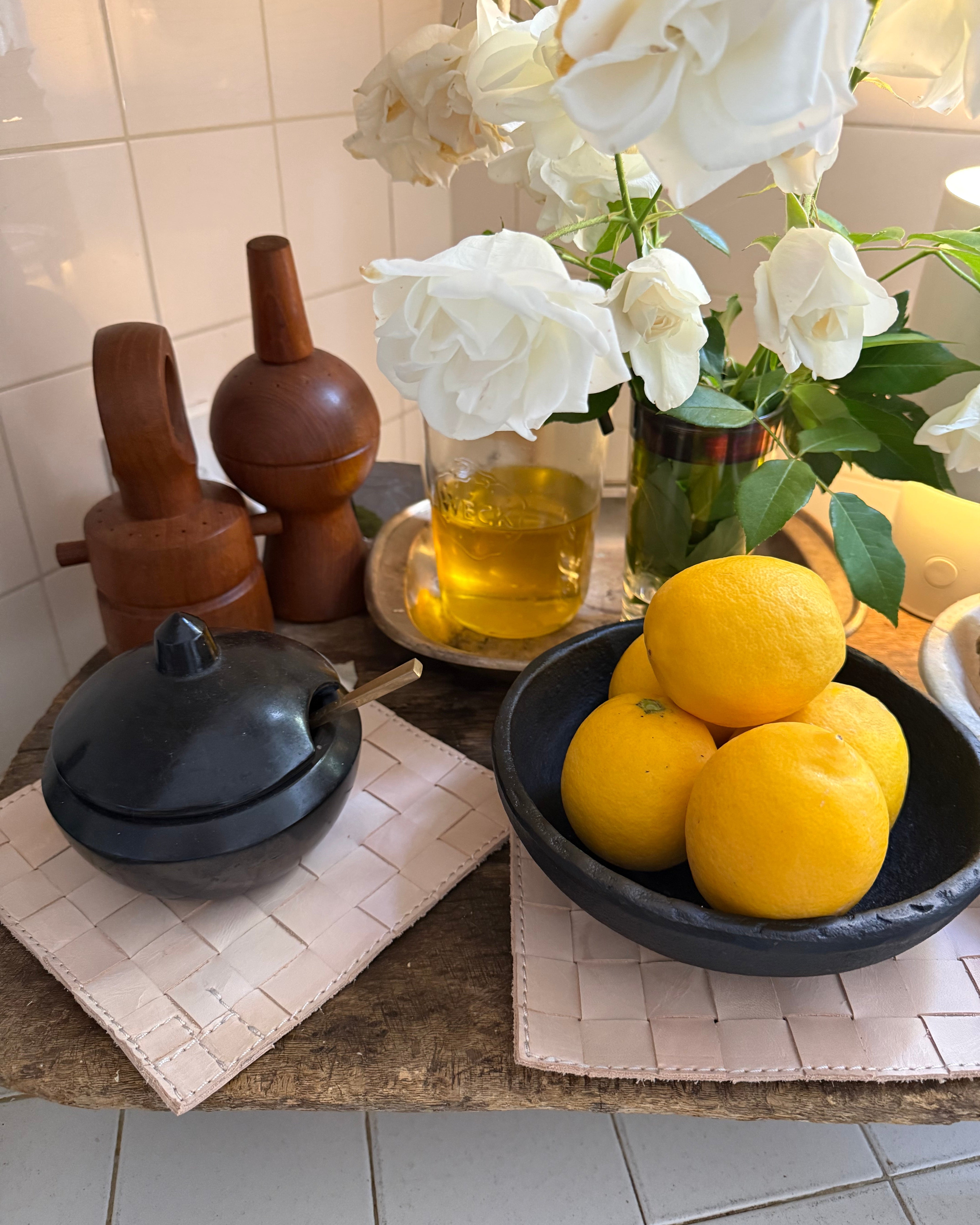 Bowl of lemons on a decorative stand with flowers and candles in the background.