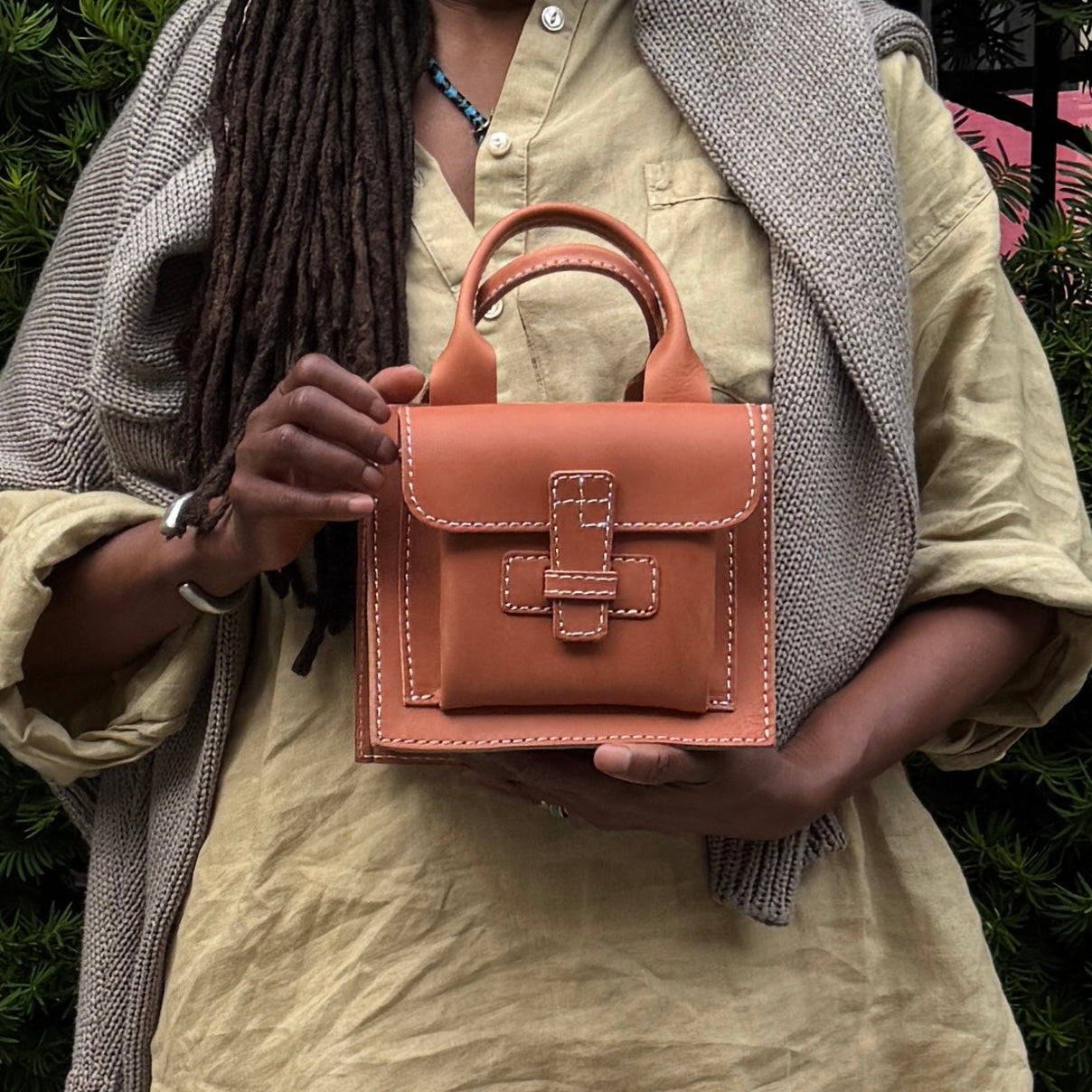 Person holding a brown leather handbag with a neutral background