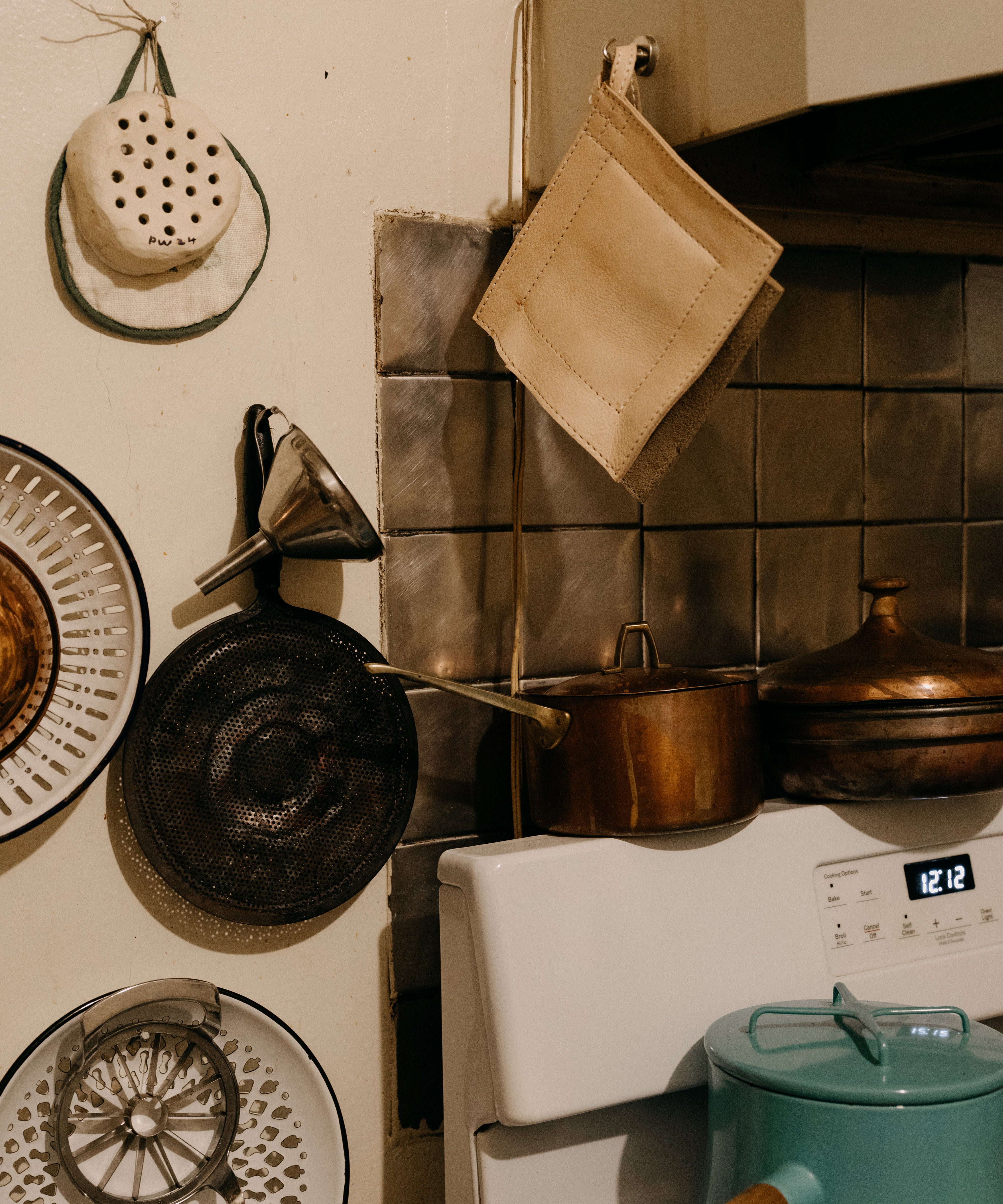 Kitchen stove with pots, pans, and a teal pot on a tiled wall.