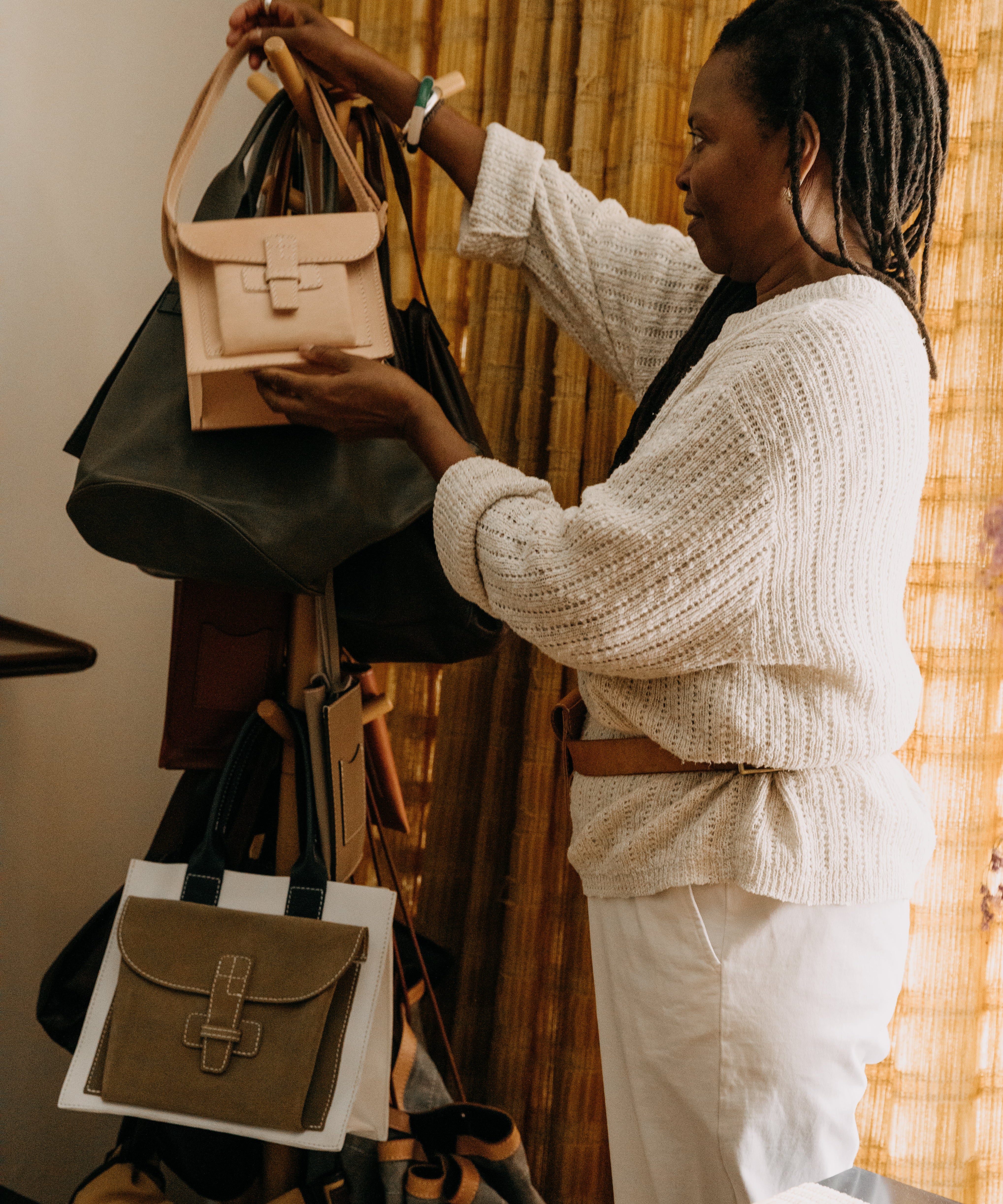 Agnes holding a beige handbag in front of a rack with various bags.
