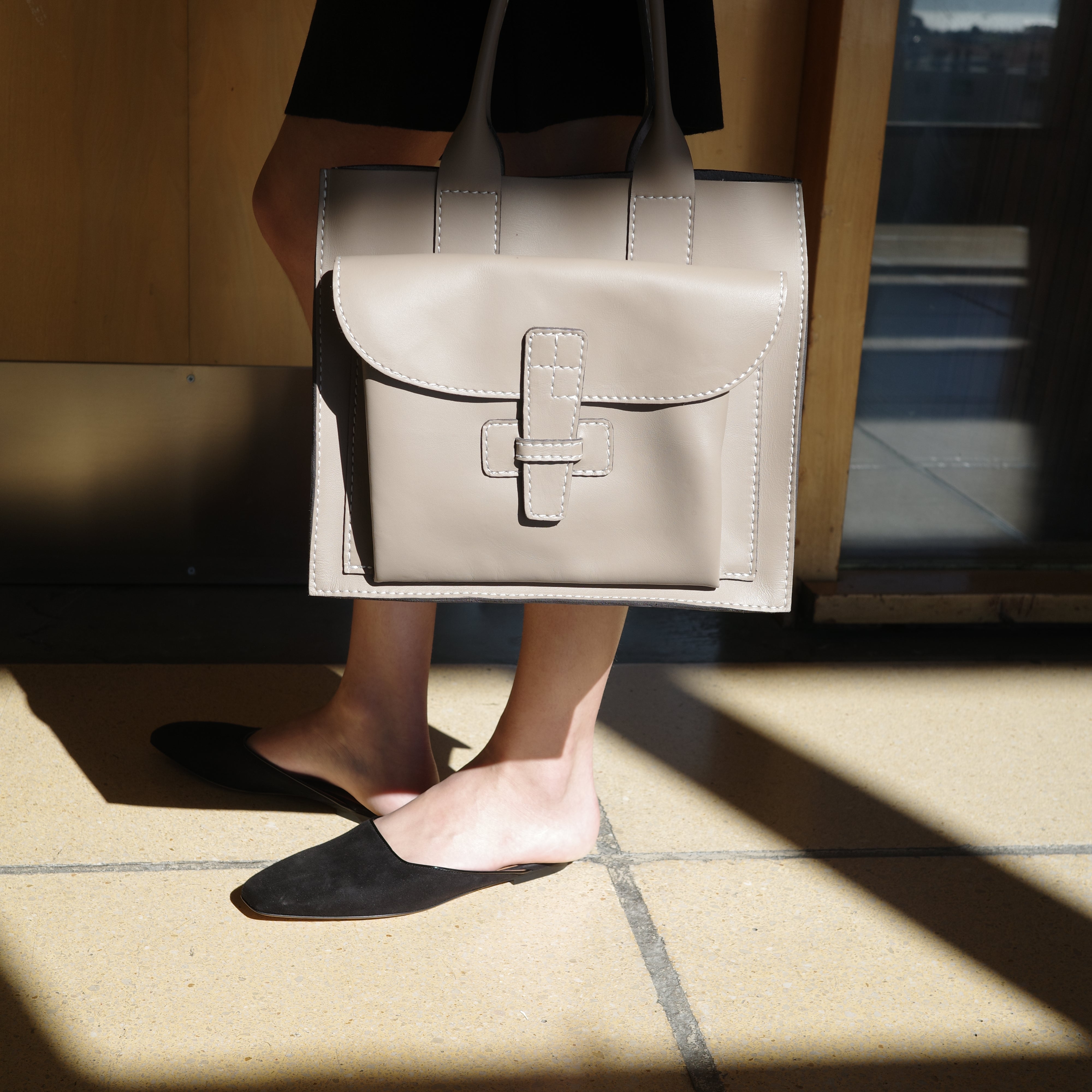 Person holding a leather taupe handbag with a reflective surface.