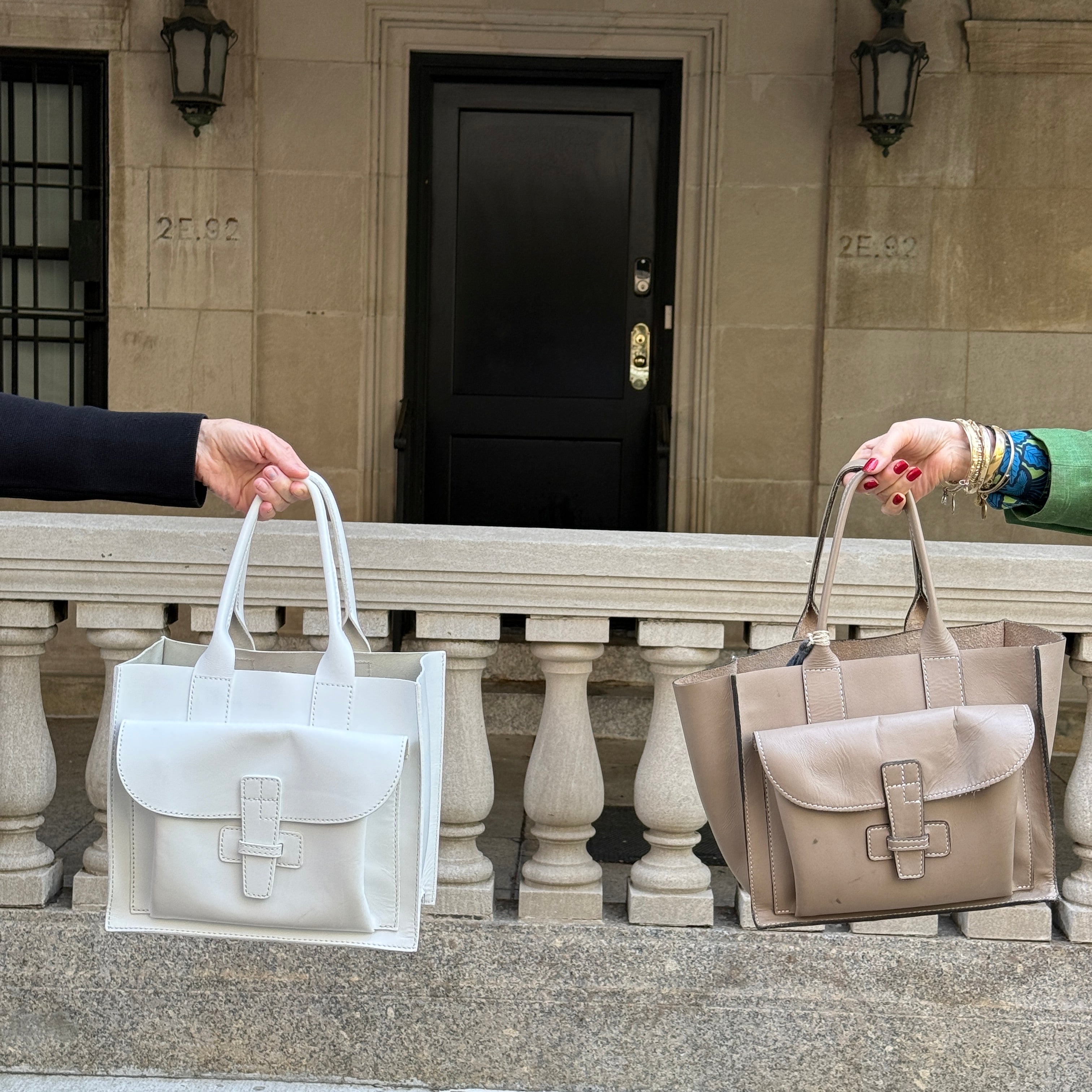 Two people holding white and beige leather handbags on a stone staircase.