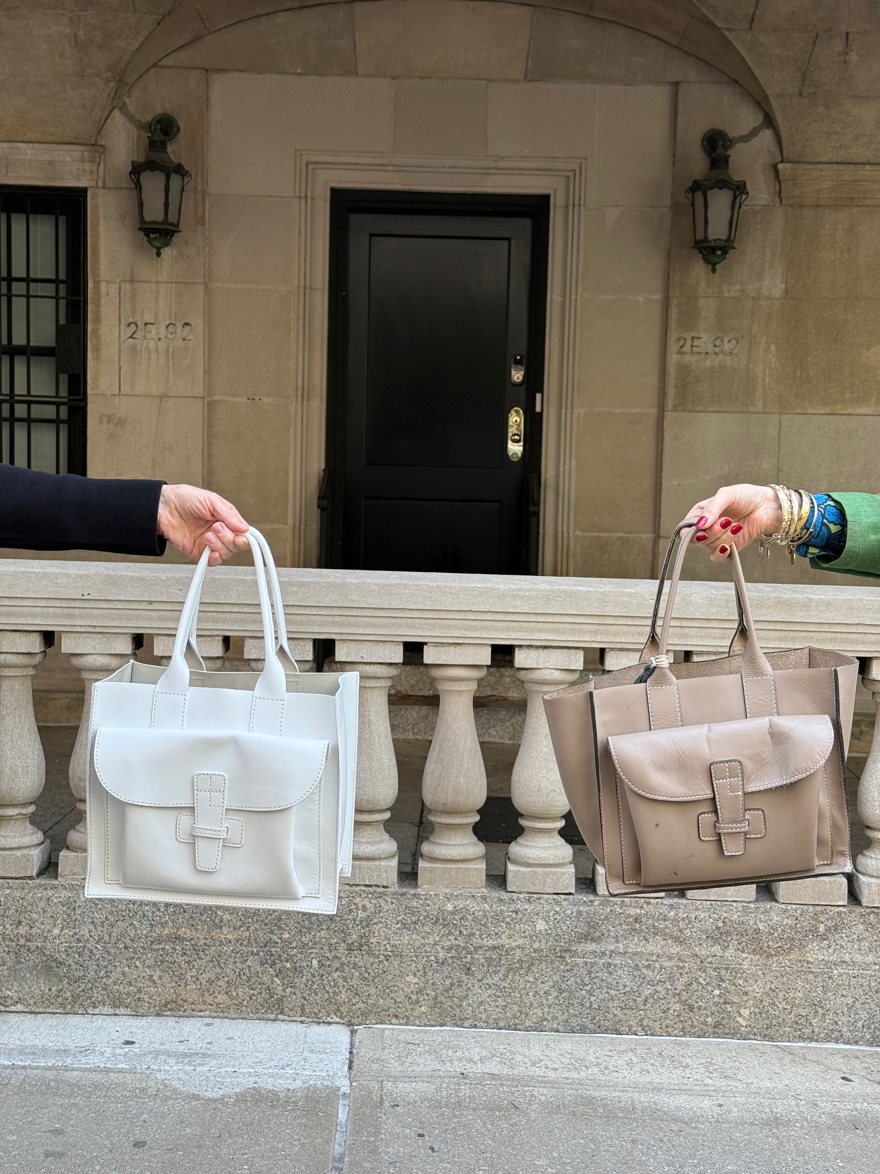 Two people holding white and beige leather handbags on a stone staircase.