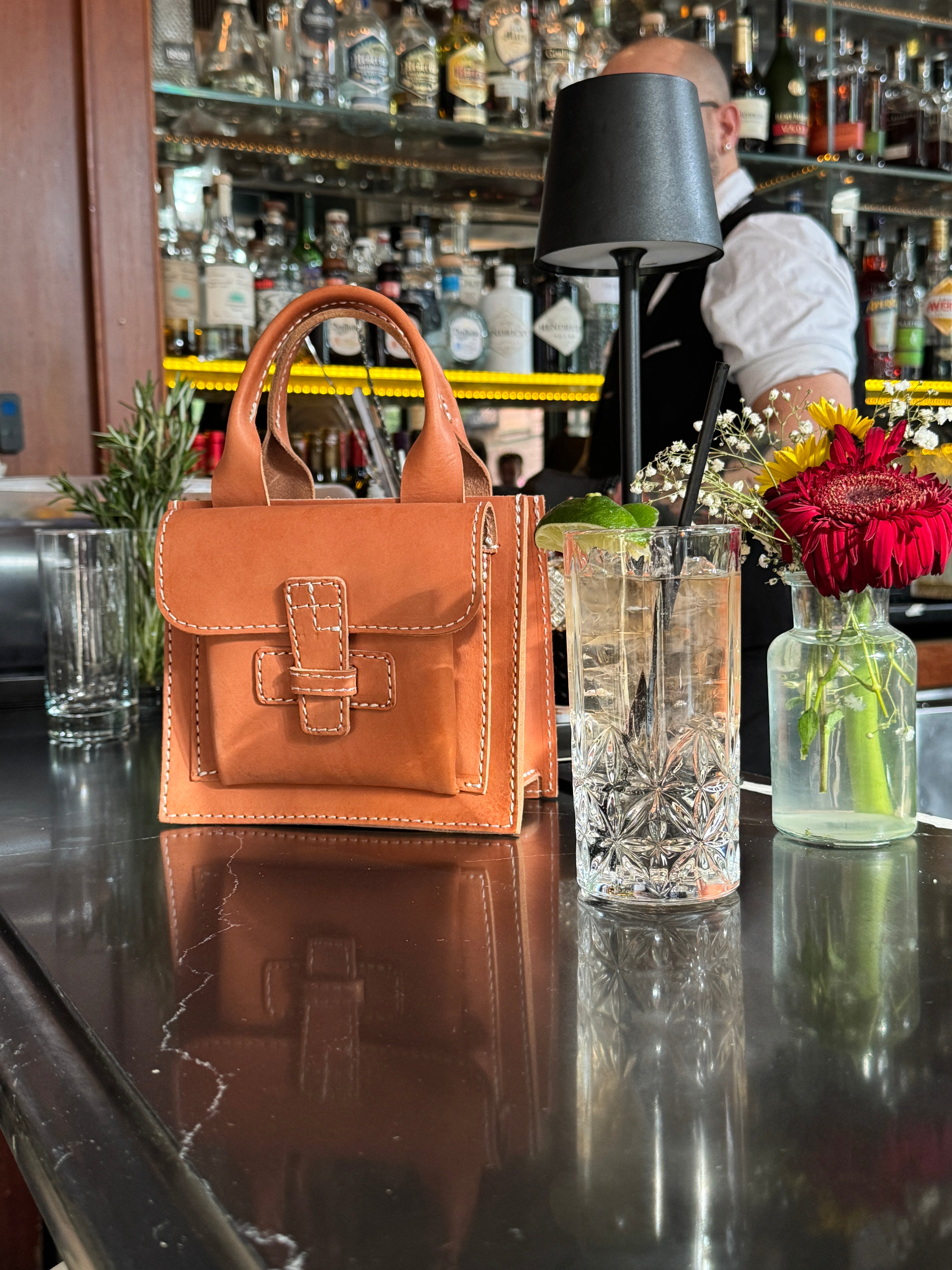 leather bag resting on a bar counter next to a glass of water. 