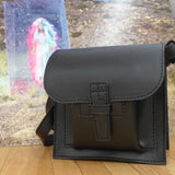 Black leather bag on a wooden floor with a colorful abstract painting in the background.