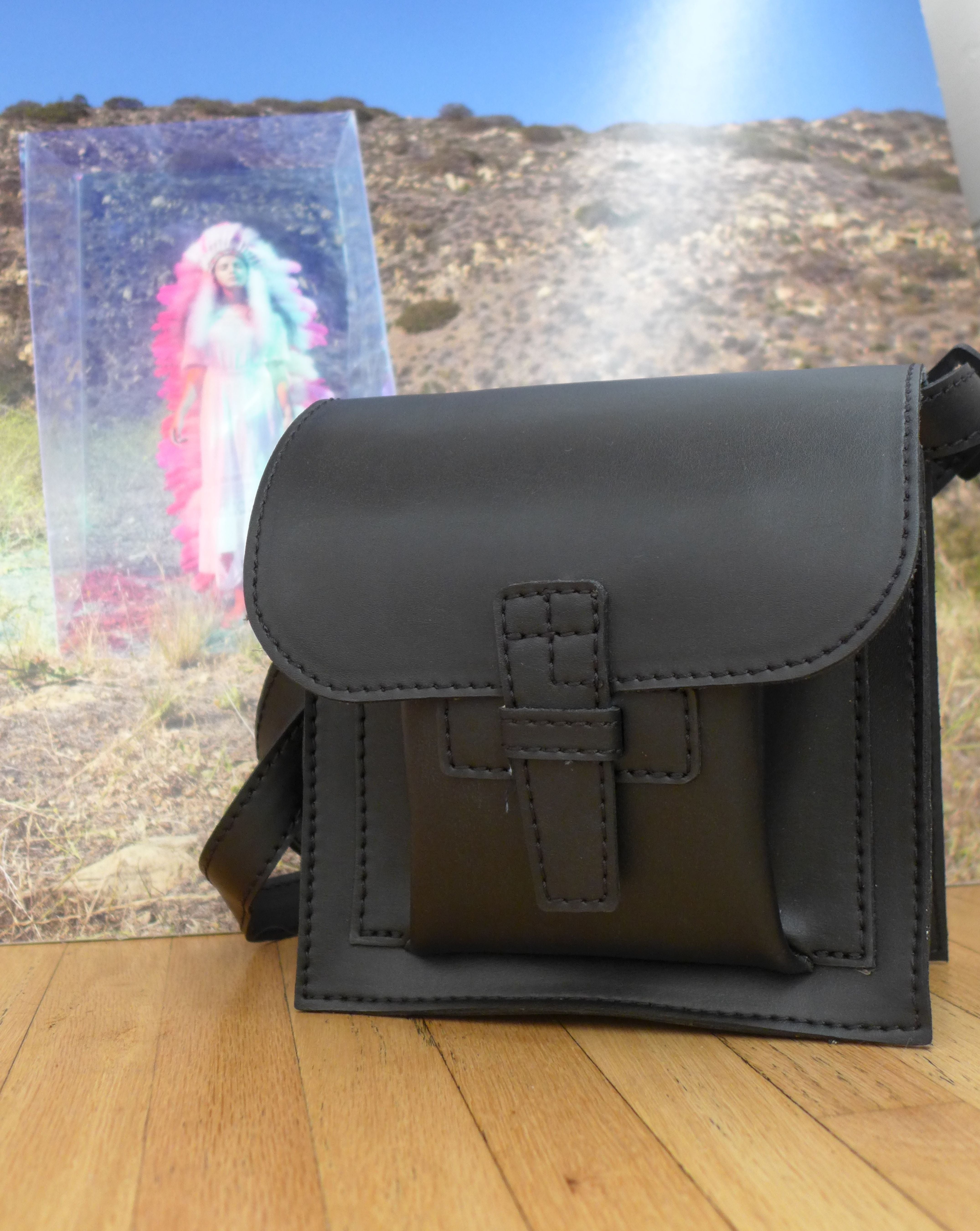 Black leather bag on a wooden floor with a colorful abstract painting in the background.