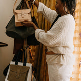 Agnes holding a beige handbag in front of a rack with various bags.