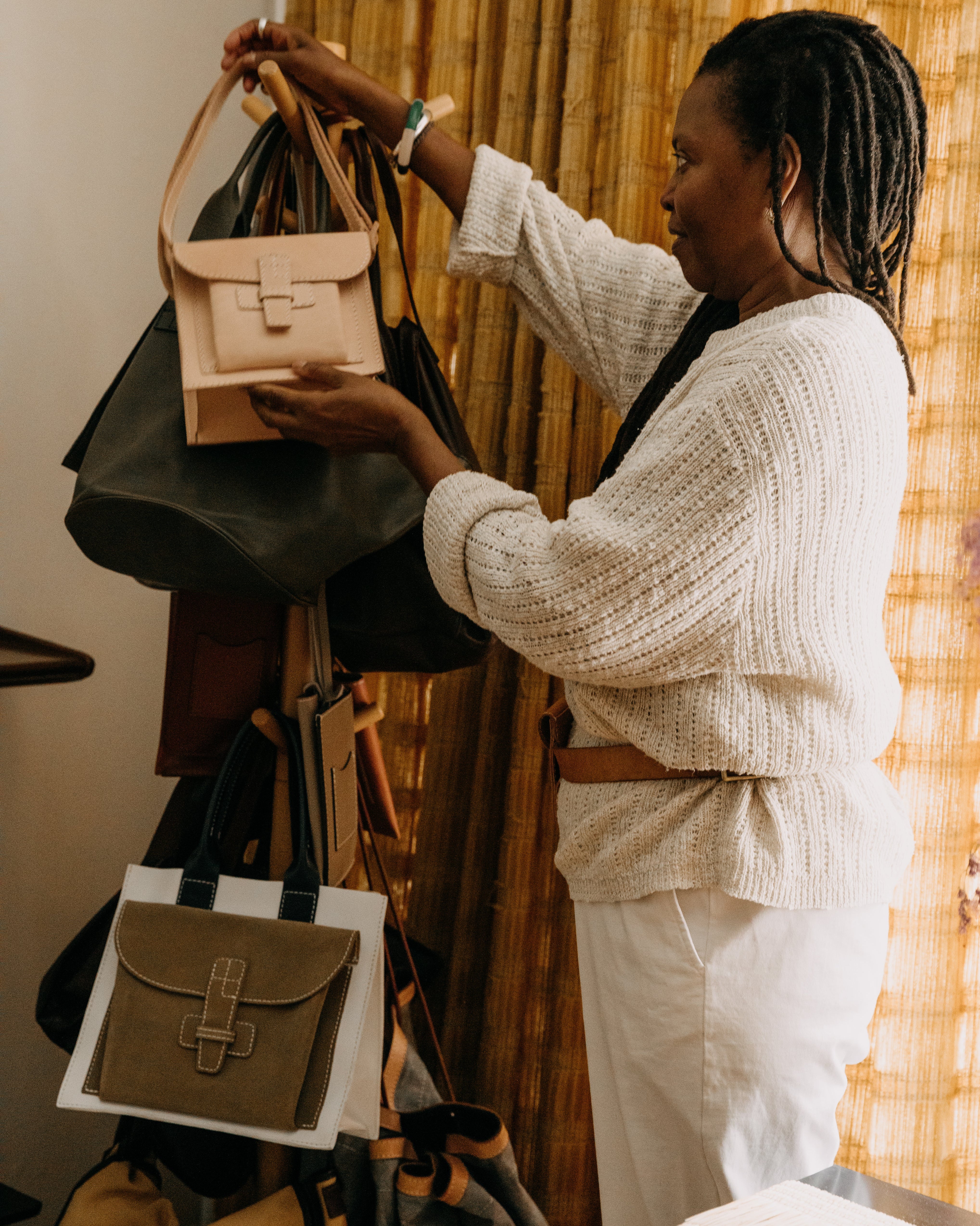 Agnes holding a beige handbag in front of a rack with various bags.