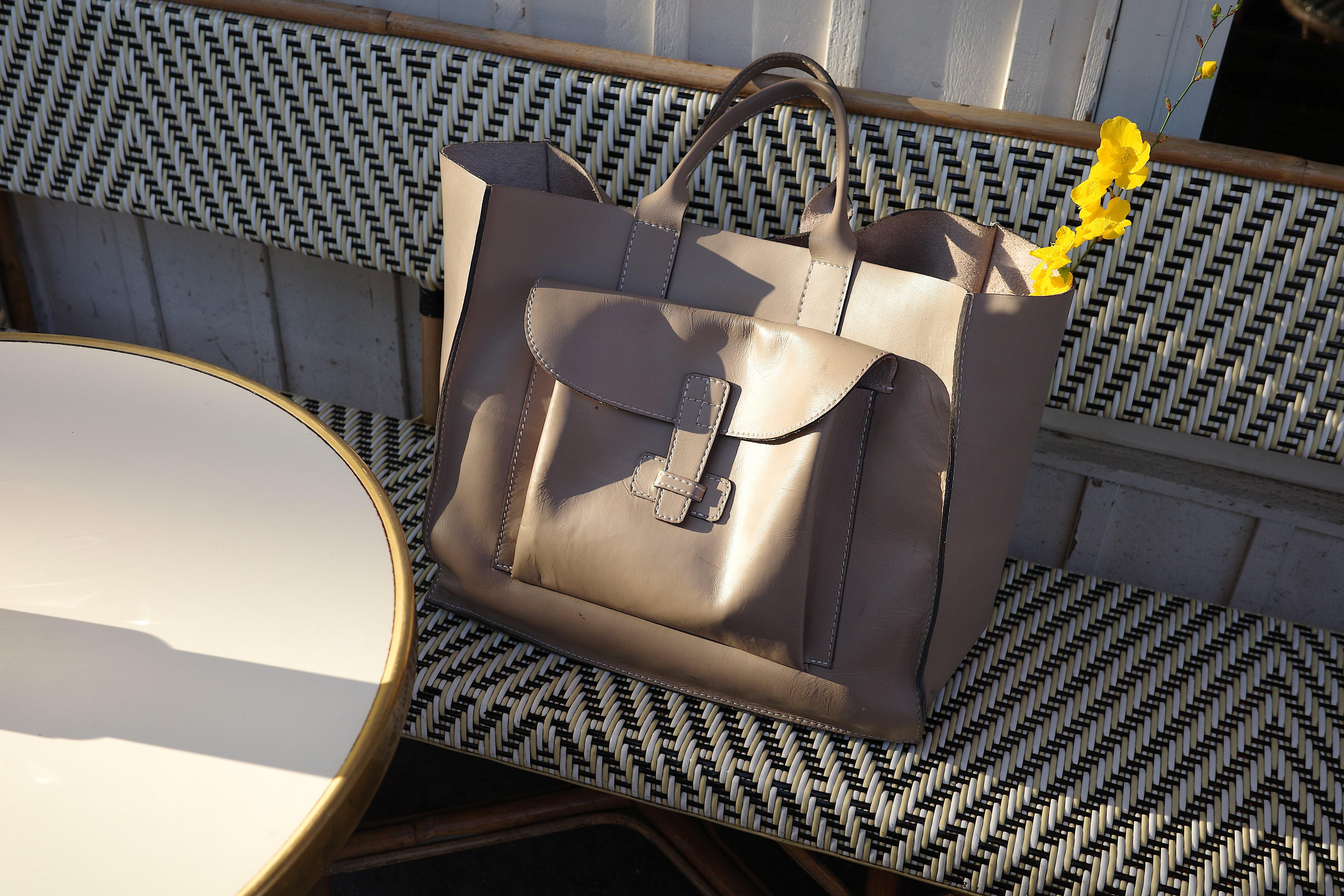 Taupe leather bag on a patterned bench with yellow flowers resting in the bag.